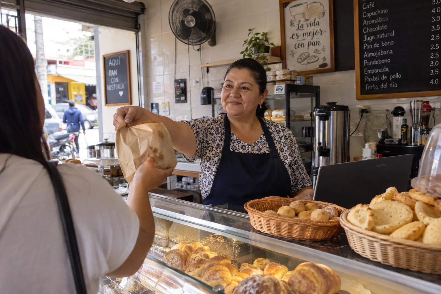 Panadera atendiendo a una clienta en un negocio colombiano